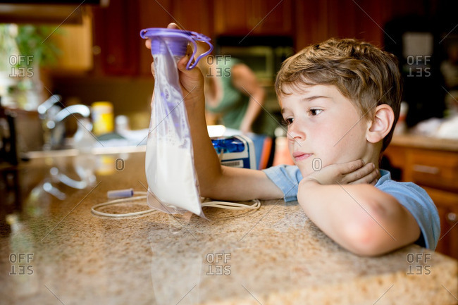 A boy holding feeding tube bag