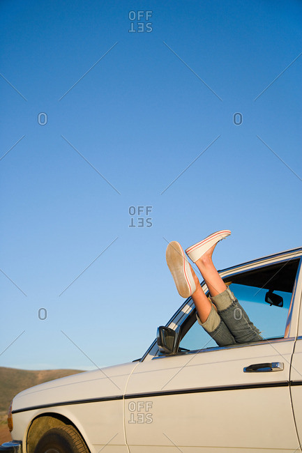 Young woman\'s feet sticking out of a car window