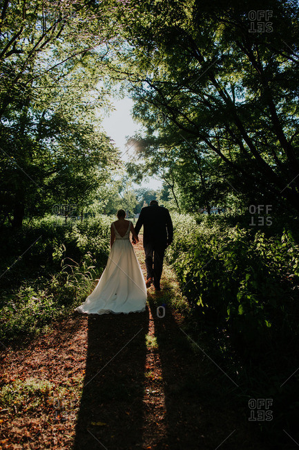 Back view of bride and groom walking on path in woods