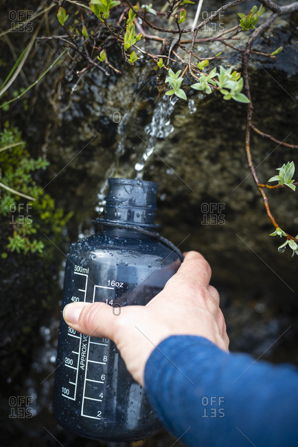 Cropped image of hiker\'s hand filling water bottle from stream