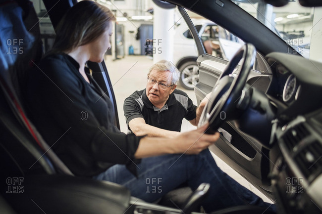 Senior expert discussing with female customer sitting in car at repair shop