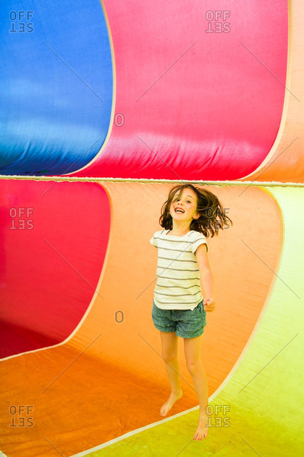 Little girl jumping inside a colorful rainbow parachute