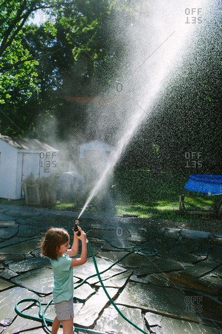 Little girl in a backyard spraying a garden hose