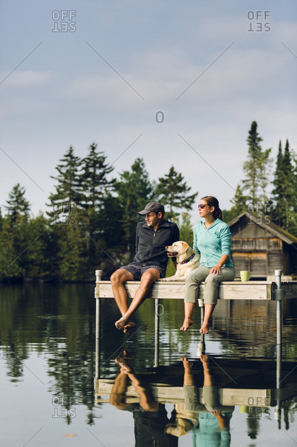 Man And Woman With Their Dog Relaxing On Edge Of Dock On Caspian Lake