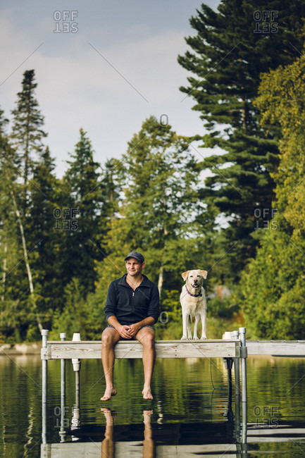 Smiling Man And Dog Sitting On Edge Of Dock On Caspian Lake