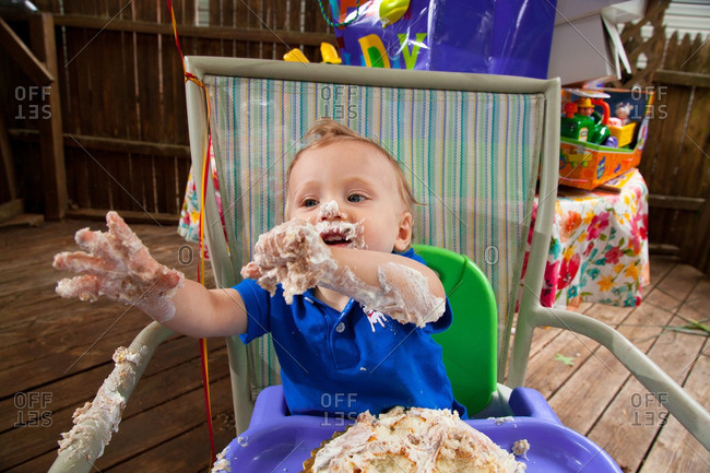Young Caucasian boy celebrates his first birthday making a mess with Cake outside during Summer