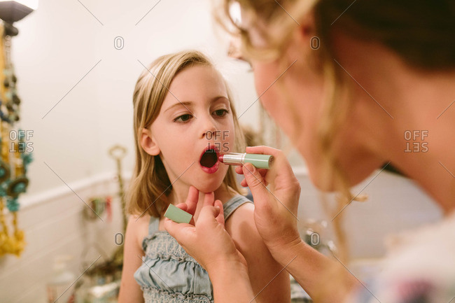 Girl holds still while her mother applies lipstick to her lips