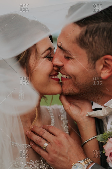 Newly married couple smiling and kissing beneath the bride\'s veil