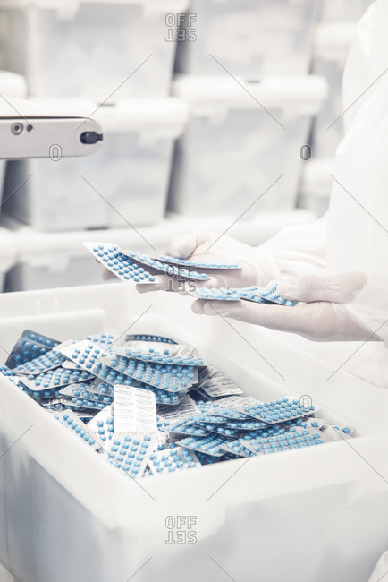 Worker inspecting pill packets exiting production equipment