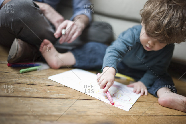 Toddler boy sitting on floor with parent, drawing on paper