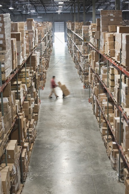 Hispanic man moving boxes with hand truck in warehouse