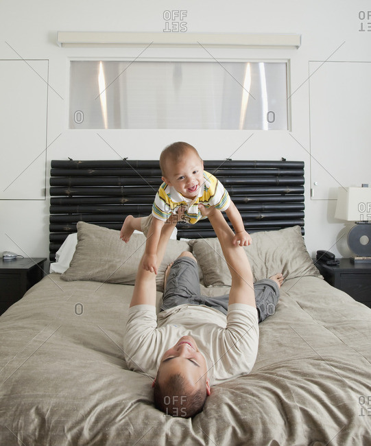 Father lifting son on bed in bedroom