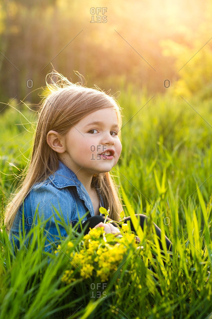 Little girl sitting in a field holding yellow flowers
