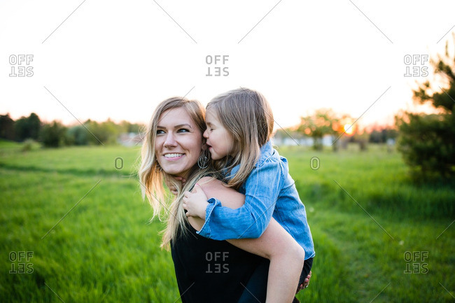 Little girl telling her mother a secret while getting a piggy back ride