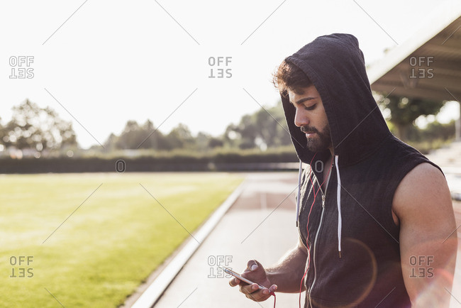 Young man with cell phone wearing hooded top on tartan track
