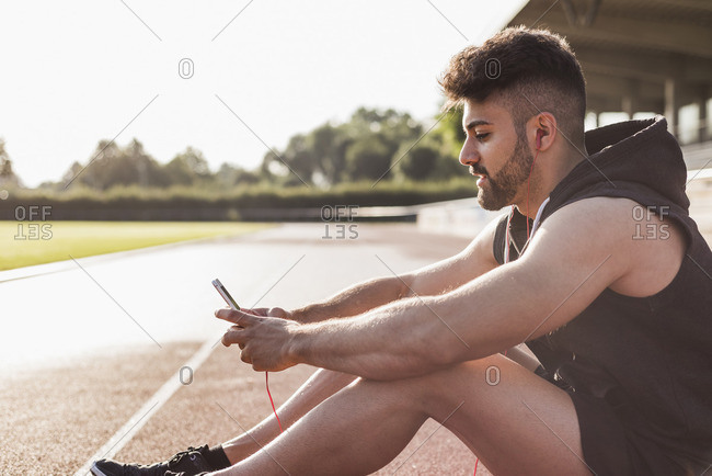 Young man with cell phone sitting on tartan track