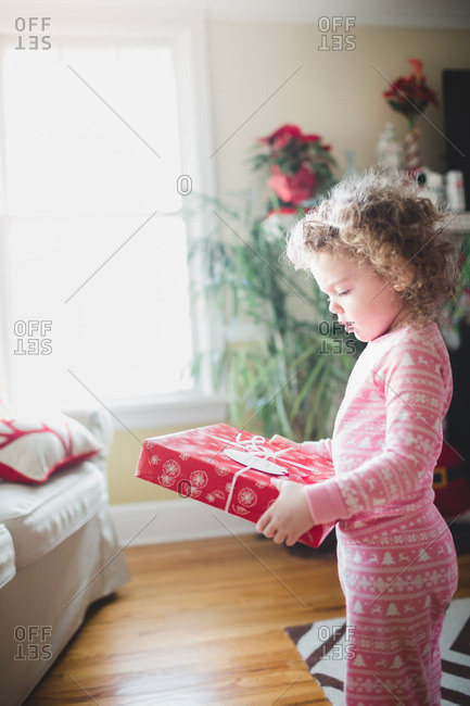 Toddler girl standing with gift in living room on Christmas morning