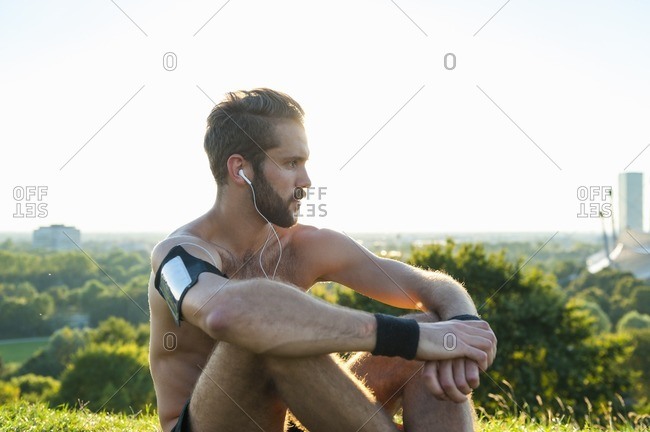 Athlete sitting on a meadow listening to music after workout