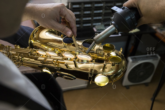 Instrument maker heating with a machine the keys of a saxophone during a repair