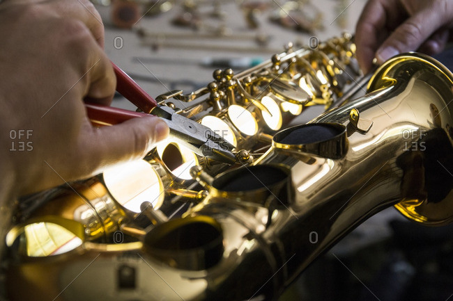 Instrument maker dismounting a saxophone using pliers during a repair