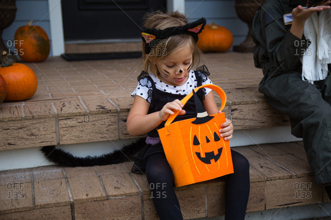 Girl in cat costume peering into trick or treating bag on porch stairway