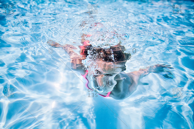 Girl swimming underwater in sunlit swimming pool