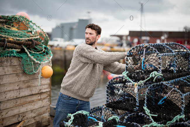 Young fisherman stacking lobster pots in harbor, Fraserburgh, Scotland
