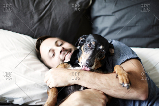 Young man reclining on bed hugging dog