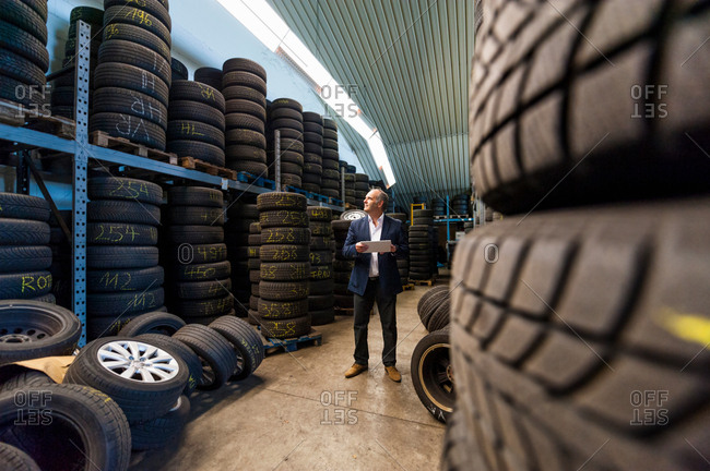 Senior business owner with digital tablet counting stacked tires in garage