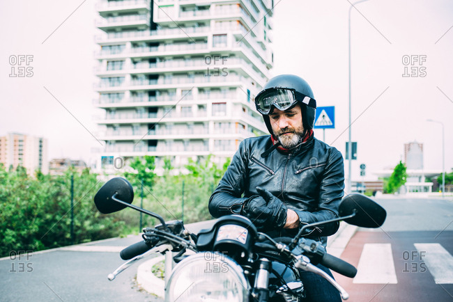 Mature male motorcyclist sitting on motorcycle putting on gloves