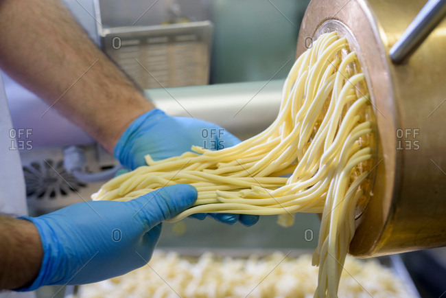 Worker with spaghetti coming out of machine in pasta factory