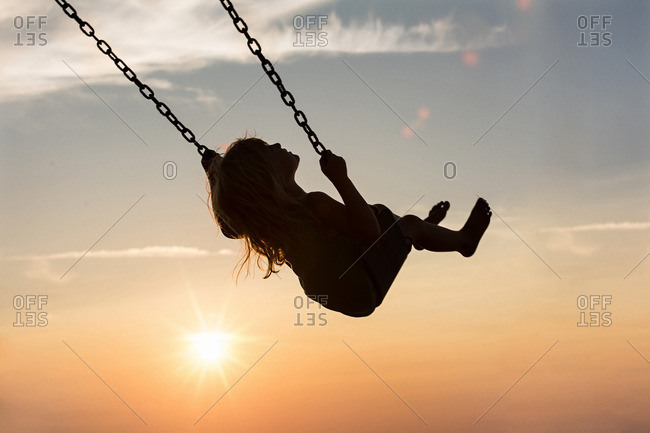 Little girl swinging on a swing at sunset