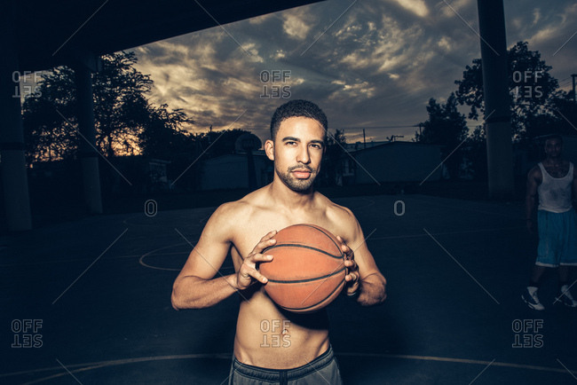 Bare chested man on basketball court holding basketball looking at camera