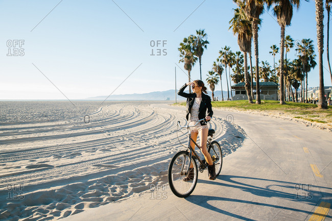 Young woman cycling at beach looking out to sea, Venice Beach, California, USA