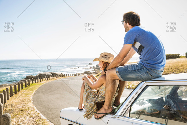 Mid adult couple looking out from on top of car on coast road, Cape Town, South Africa