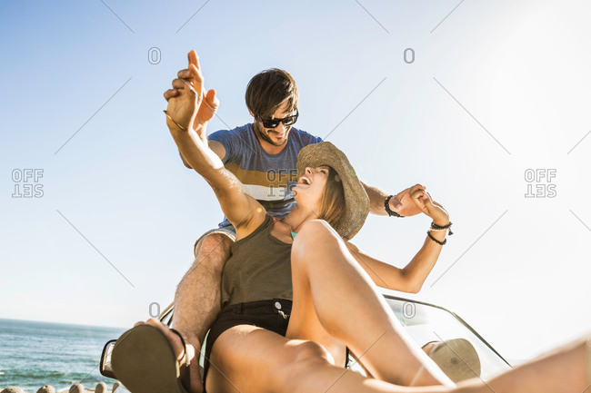 Mid adult couple holding hands on top of car on coast road, Cape Town, South Africa