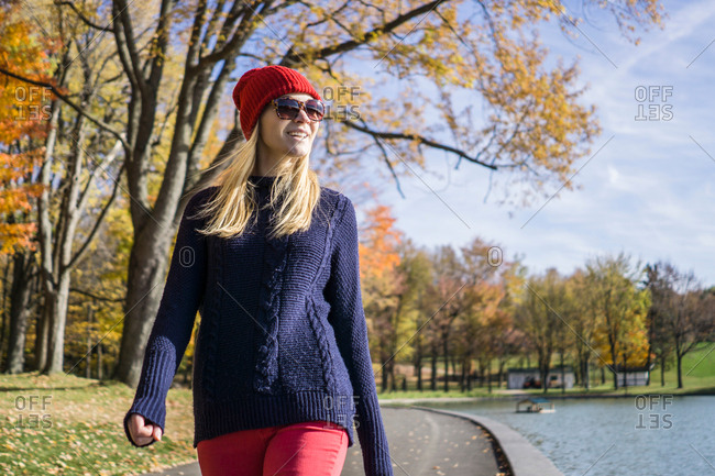 Stylish young woman wearing red knitted hat strolling in park