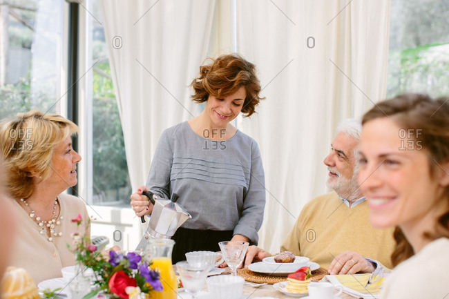 Senior Italian parents and adult daughters pouring coffee at breakfast table