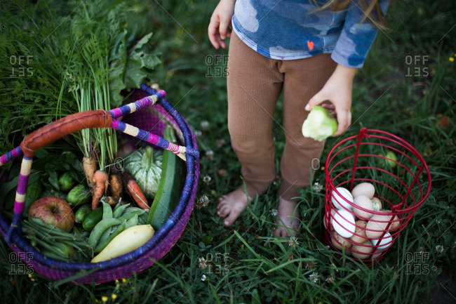 Girl standing outside next to a basket of eggs and a basket of fruits and veggies