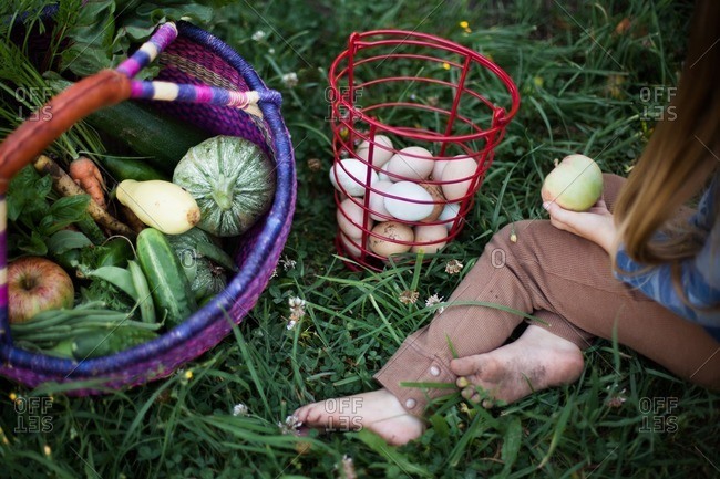 Girl sitting outside next to a basket of eggs and a basket of fruits and veggies