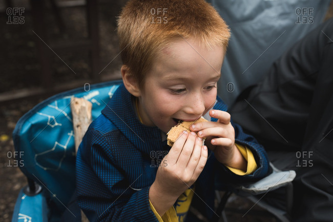 Boy sitting in a camping chair eating s\'mores