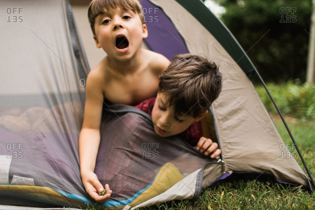 Two boys hanging from the door of a tent making silly faces