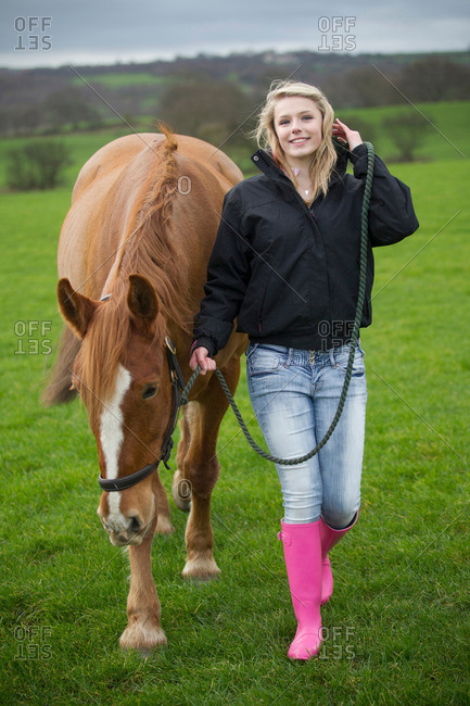 Teenage girl walking horse in field