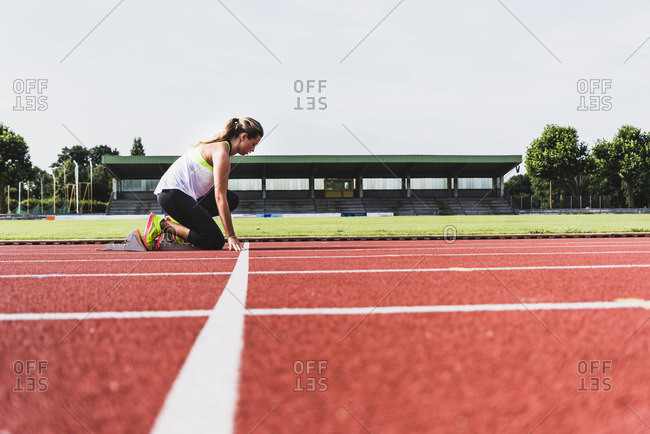 Young woman on tartan track in starting position