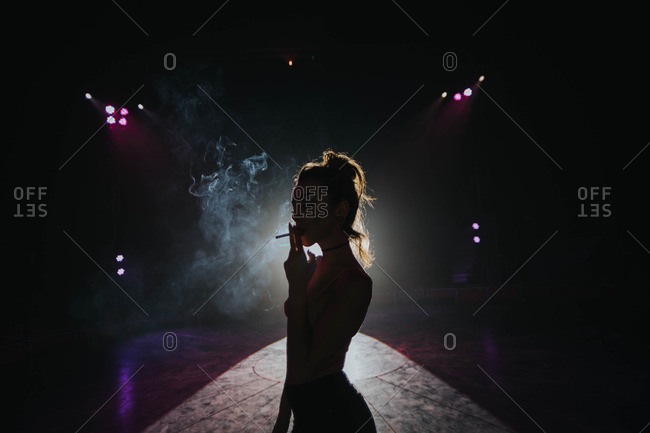 A silhouette of a woman smoking a cigarette standing in front of a projector