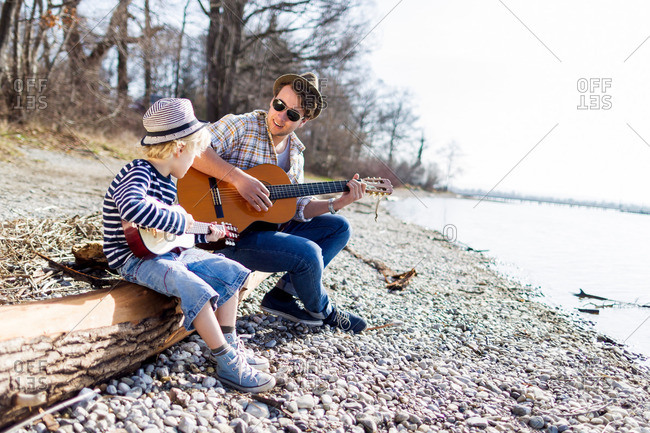 Father and son playing guitars by creek