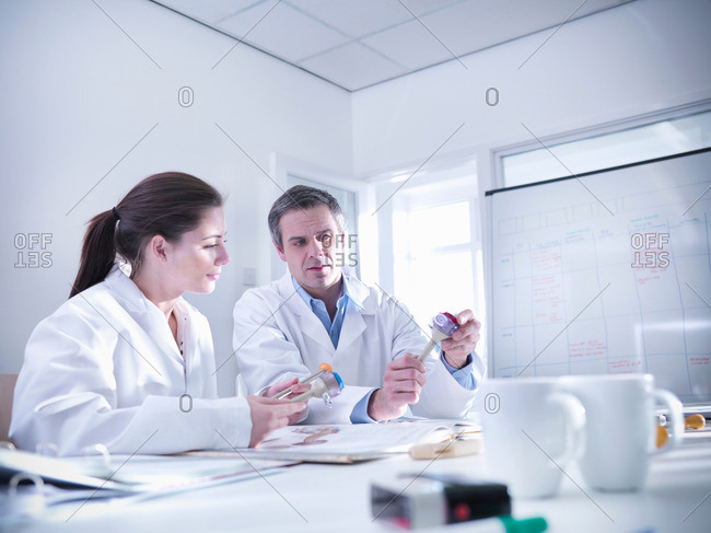 Male and female scientists in office discuss product prototypes they are holding.