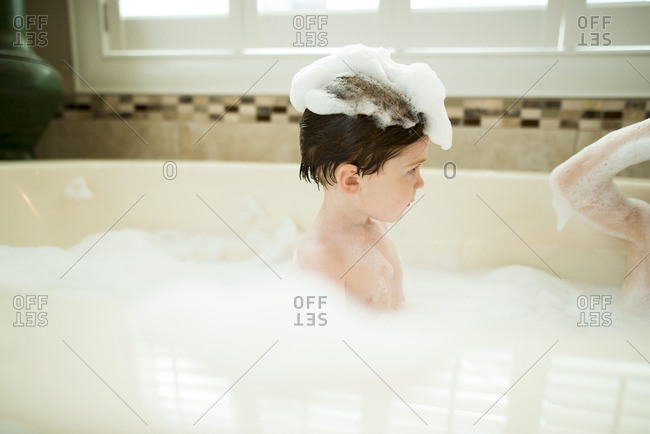 Young boy in tub with bubbles on his head