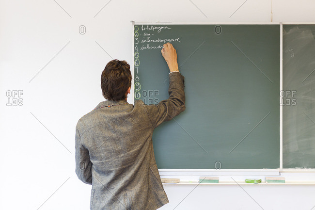A biology teacher writing on a chalk board during a class