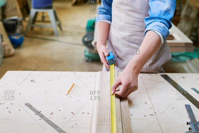 Close up of a man using a tape measure to measure the length of a board in his workshop